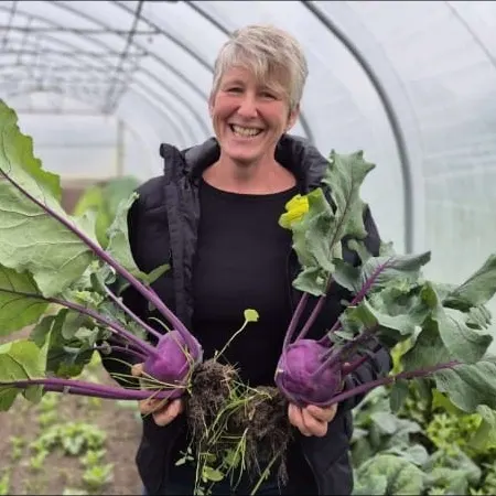 Lachend im Folientunnel, in jeder Hand ein frisch geernteter lila Kohlrabi